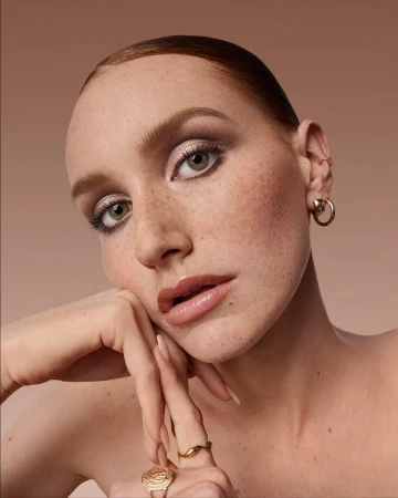 Close-up portrait of a woman with freckles and gold jewellery resting her chin on her hands by Felisha Tolentino.