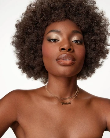 Close-up beauty portrait of a Black woman with voluminous afro hair wearing gold layered necklaces against a white background.