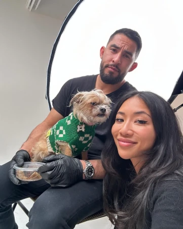 Three people and a dog in a green sweater pose in a bright photo studio, with one person holding a container of dog food.