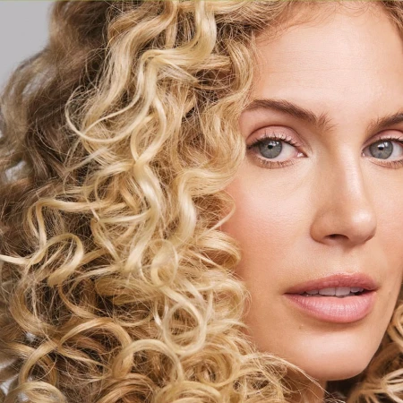 Close-up of a woman's face with blonde curly hair. Beauty portrait showcasing makeup and hair.