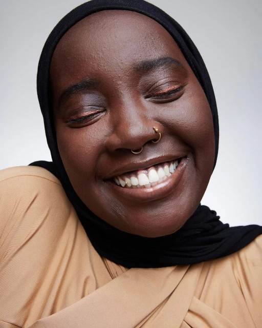 Close-up portrait of a smiling African American woman in a hijab, showcasing a joyful expression, clear skin, and minimal jewelry.