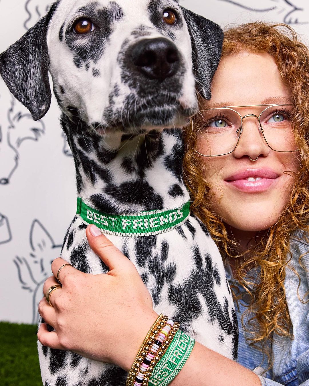 Woman with curly red hair hugs a dalmatian dog wearing a green collar with text 'BEST FRIENDS', dog drawing background.