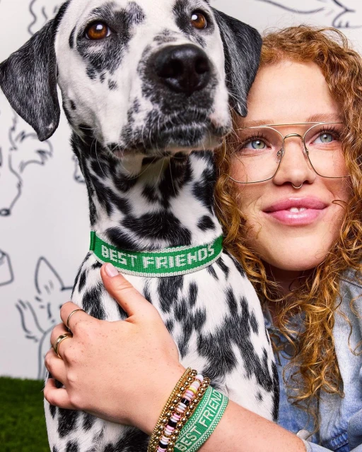 Woman with curly red hair hugs a dalmatian dog wearing a green collar with text 'BEST FRIENDS', dog drawing background.