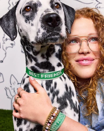 Woman with curly red hair hugs a dalmatian dog wearing a green collar with text 'BEST FRIENDS', dog drawing background.