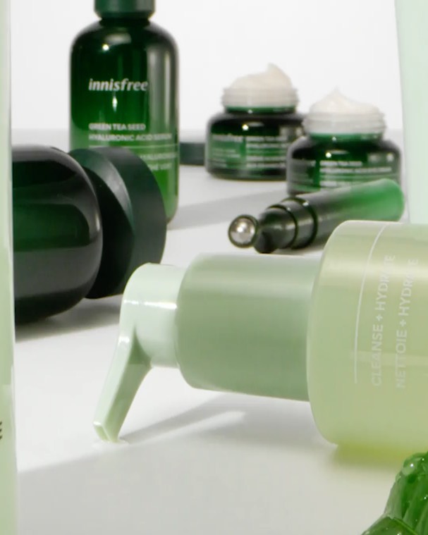 Close-up product shot of various green-toned skincare items on a white surface including bottles, jars, and tubes from Innisfree.