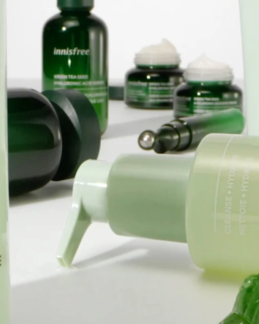 Close-up product shot of various green-toned skincare items on a white surface including bottles, jars, and tubes from Innisfree.