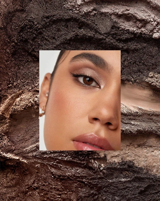 Close-up of a woman's face featuring bronze eyeshadow makeup against a brown eyeshadow powder background, shot in a photo studio.