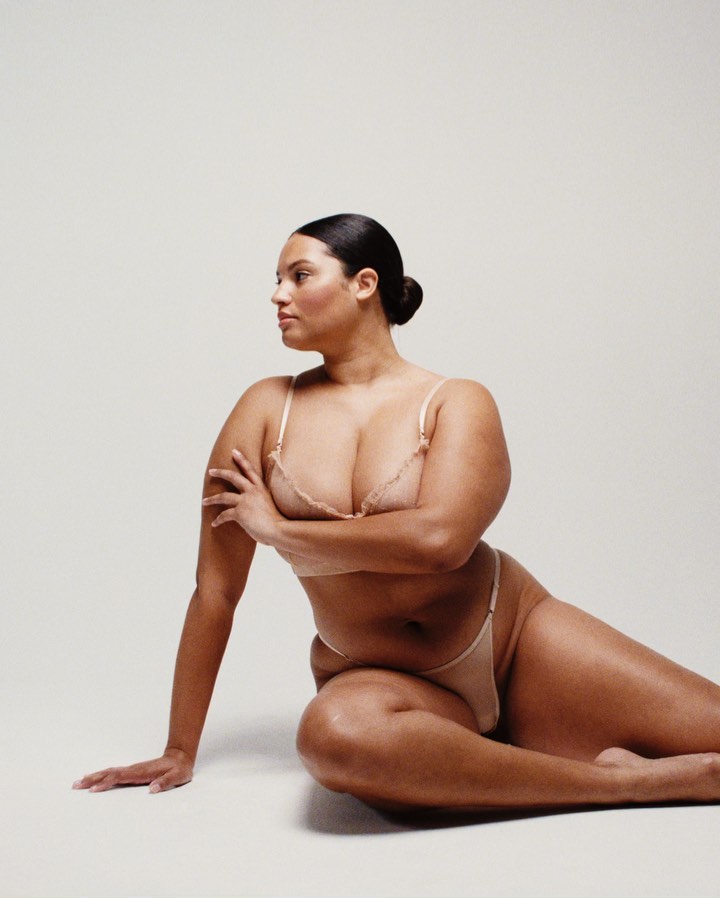 Woman in lingerie poses in a photo studio against a neutral background, showcasing a natural and confident aesthetic.