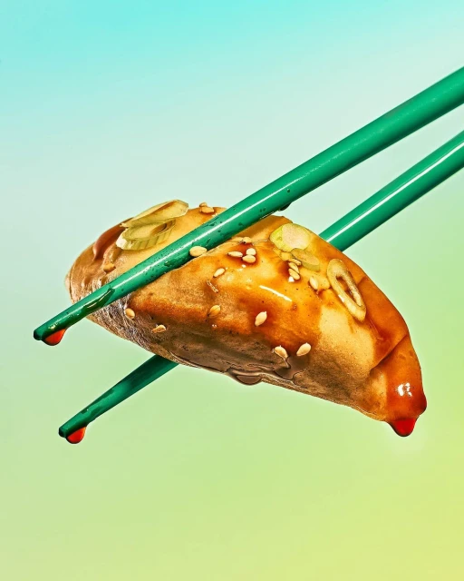 Close-up of a dumpling held by green chopsticks with visible sauce drizzle and sesame seeds against a colorful background gradient.