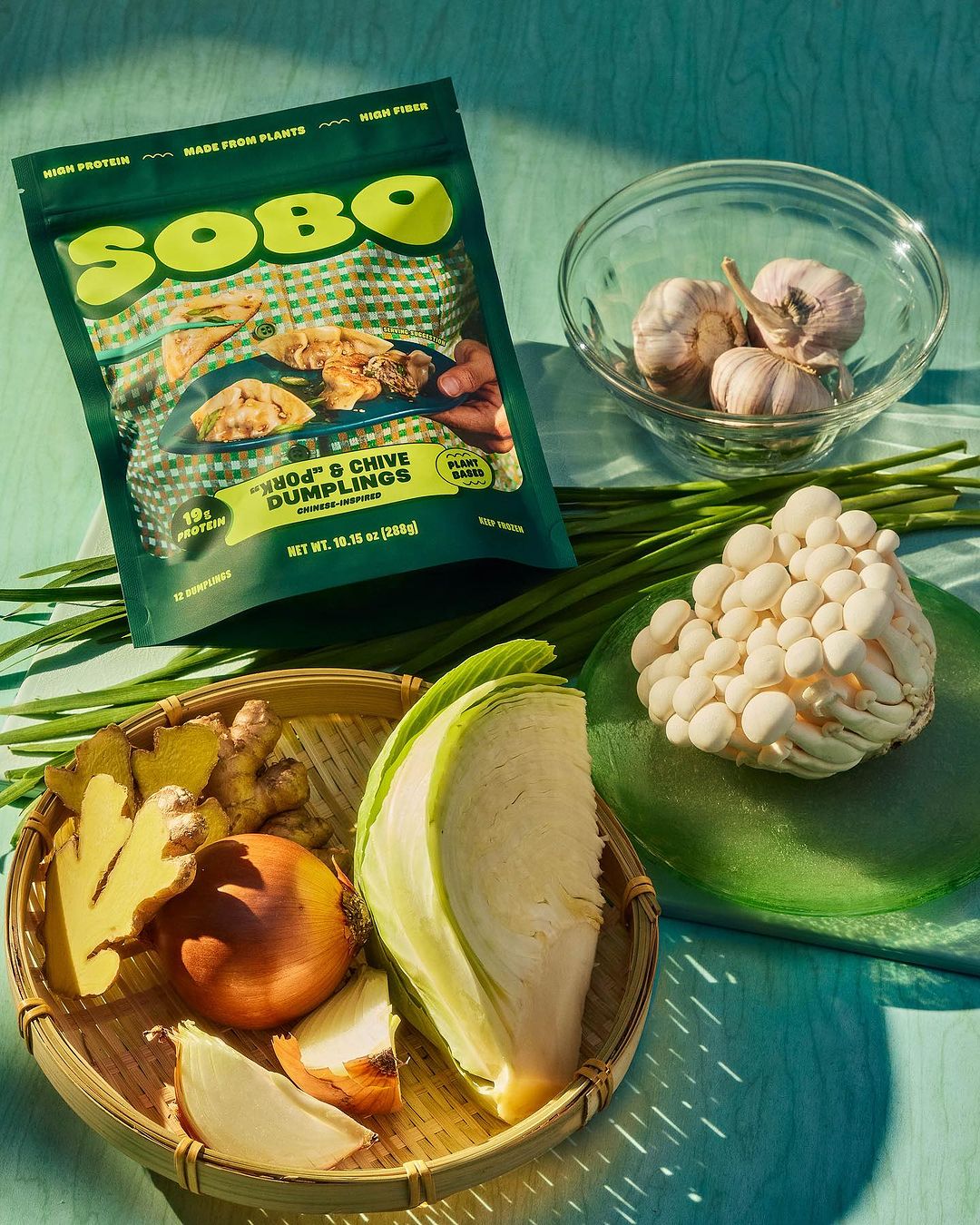 SOBO dumpling package with ingredients like onion, garlic, cabbage, mushrooms, and ginger on a green surface in bright light.