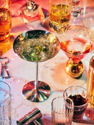 Overhead view of a reflective metal cocktail glass and assorted glassware filled with colorful drinks on a table.