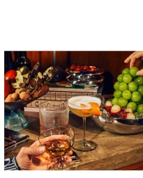 Cocktail glass with orange peel garnish alongside glasses of drinks and bowls of grapes and lychees