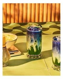 Tall layered iced beverage with green matcha base, white milk, and blue butterfly pea flower on top in ribbed glass