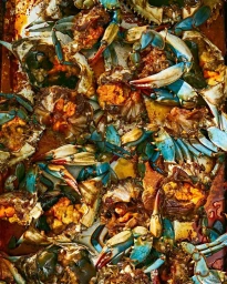Close-up overhead view of multiple prepared blue crabs with bright orange roe arranged tightly in a roasting pan.