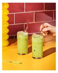 Two glasses of iced green matcha latte on an orange surface with pink tiled wall background