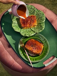 French toast served on green ceramic leaf plates on a dark green tray being drizzled with caramel from a pink jug