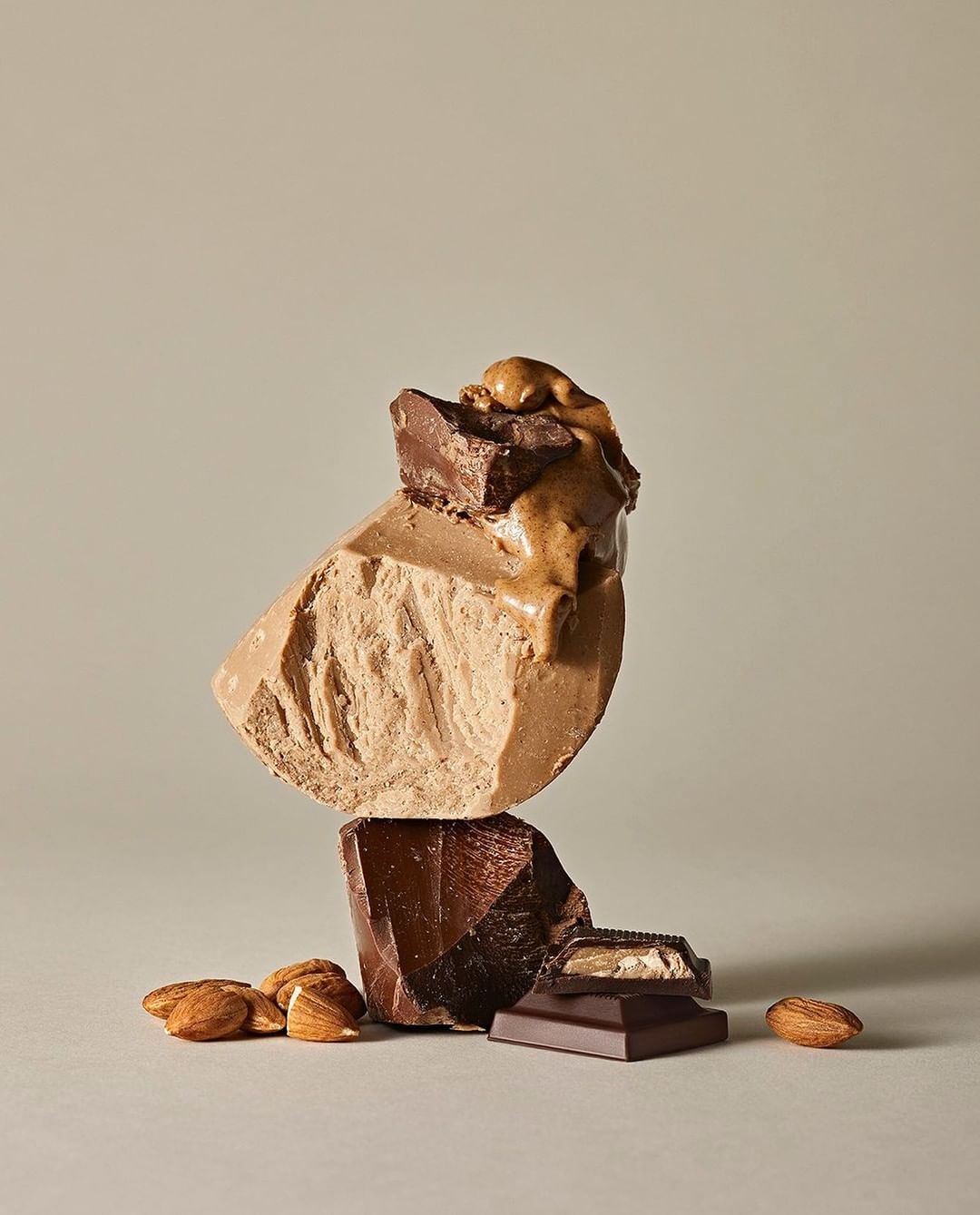 Stack of chocolate chunks with almonds, featuring milk, dark, and light chocolate on a beige background, studio lighting, food photography.