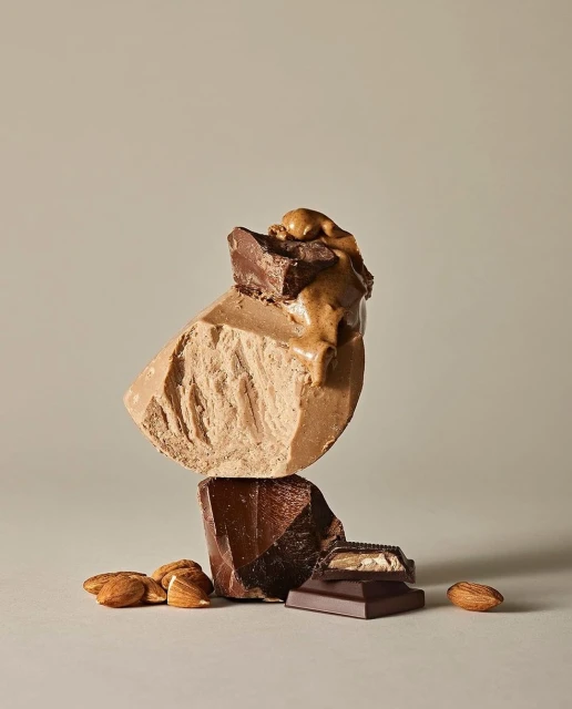 Stack of chocolate chunks with almonds, featuring milk, dark, and light chocolate on a beige background, studio lighting, food photography.