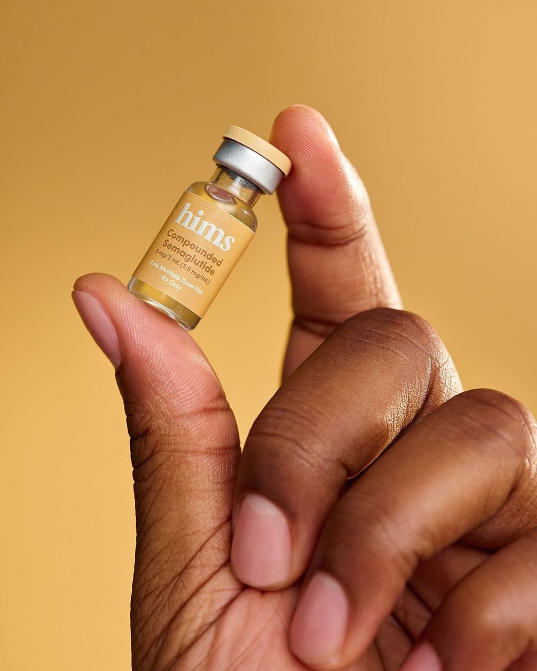 Close-up of dark-skinned hand holding small bottle of semaglutide against a yellow background, showcasing skincare or medication.