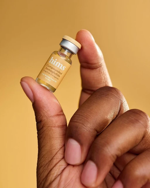 Close-up of dark-skinned hand holding small bottle of semaglutide against a yellow background, showcasing skincare or medication.