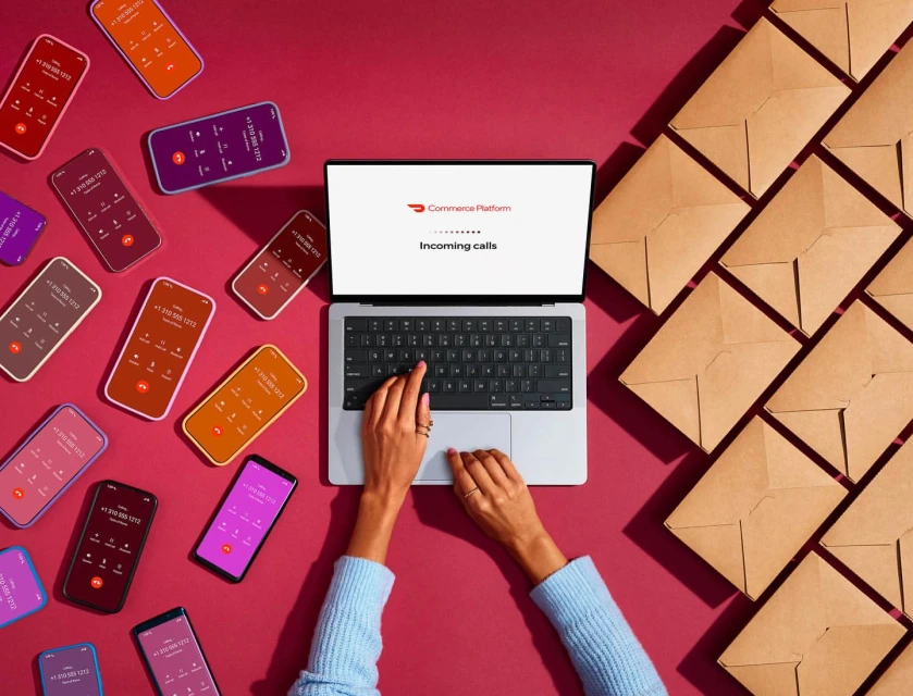 Overhead shot of laptop with 'Commerce Platform' screen, surrounded by smartphones showing call interfaces and envelopes on pink.