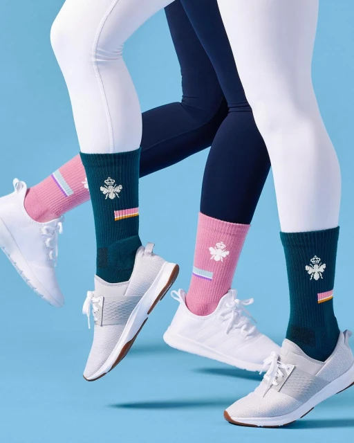 Two models showcase athletic socks with white sneakers against a light blue background in a studio fashion product shot.