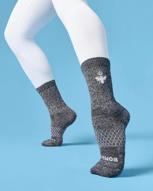 Grey socks with a white logo on a blue background, styled on mannequin legs with white leggings, emphasizing design and comfort.