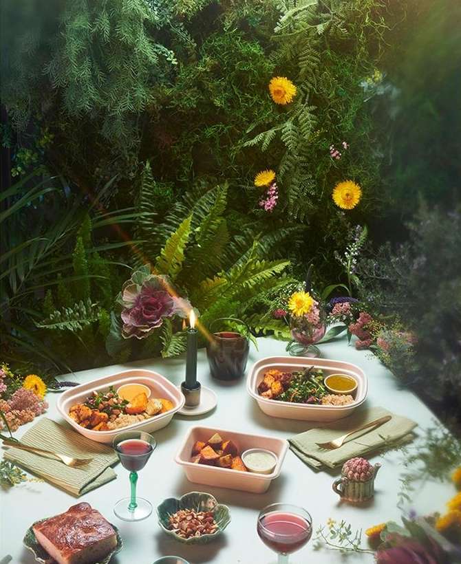 Overhead shot of an elegantly set table with bowls of food, drinks, and a candle, all surrounded by lush green foliage.