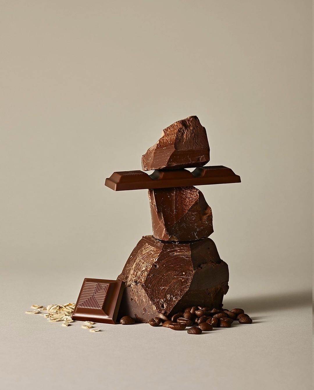 Studio shot of stacked dark chocolate pieces with coffee beans and oat flakes on a neutral background for food and beverage concept.