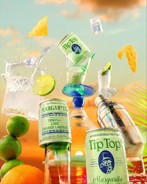 Still life of canned margaritas, cocktail shaker, glassware, limes, oranges, tortilla chips and ice against a sky background.