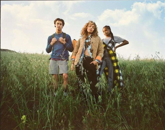 Three young models standing in a tall green meadow under an overcast sky photographed by Aaron Smith.