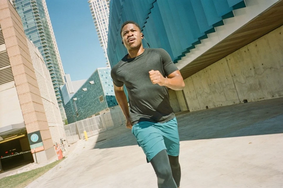 An athletic African American man is running in an urban environment on a sunny day, wearing athletic wear and headphones.