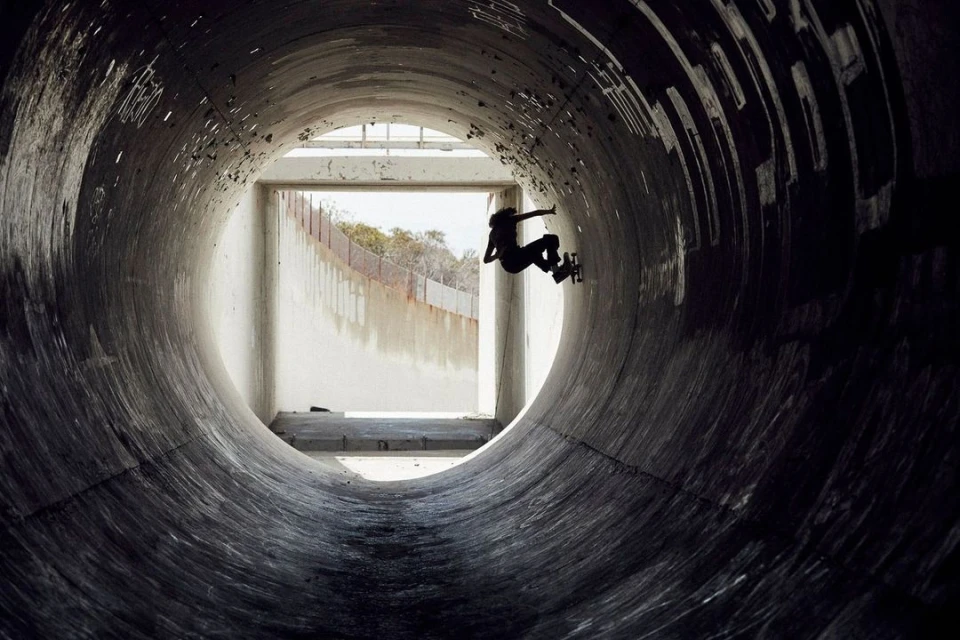 Silhouette of skateboarder riding inside a large concrete pipe with natural light coming from the tunnel entrance, urban sport lifestyle.