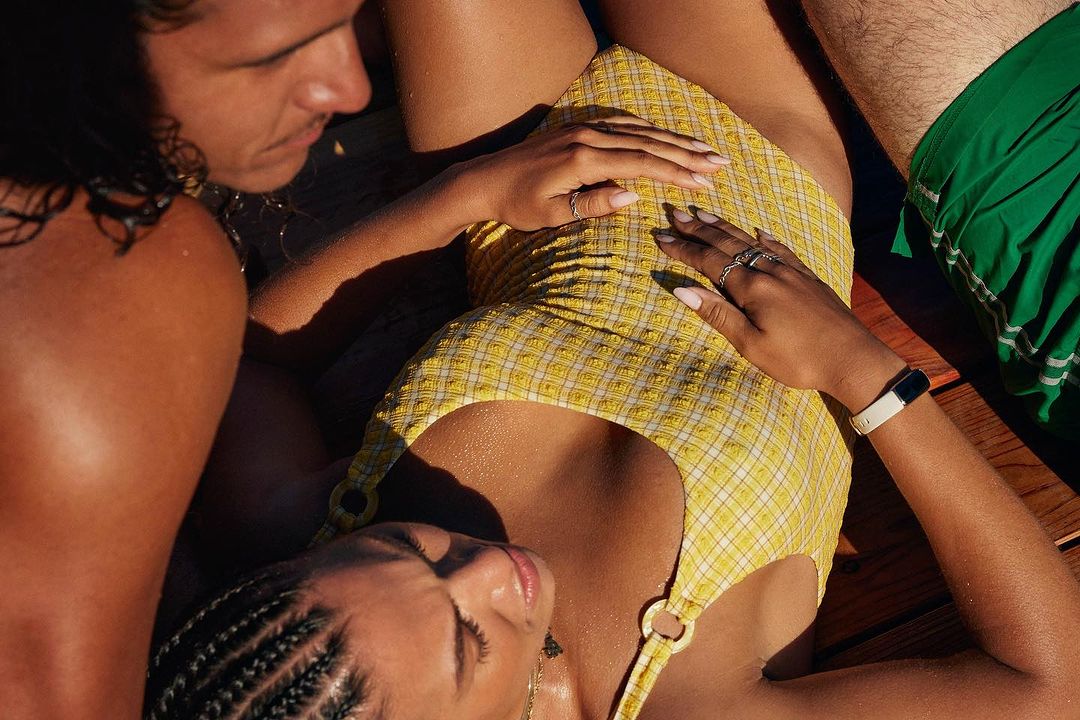 Close-up portrait of a woman wearing a yellow patterned swimsuit resting on a wooden deck next to a man.