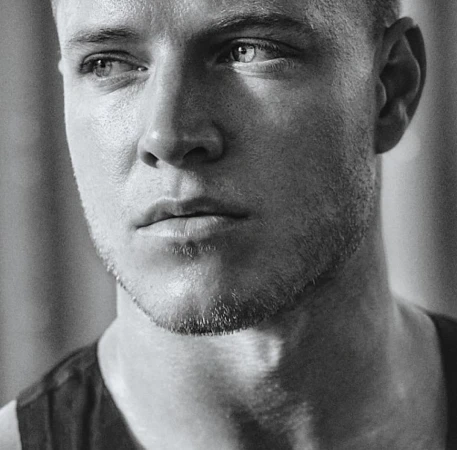 Close-up monochrome portrait of a man looking away with short hair and stubble, photographed by Aaron Smith.