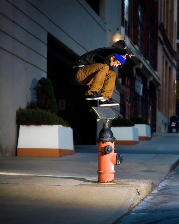 A skateboarder balances on a board placed on top of an orange fire hydrant on a city street, captured in a medium outdoor shot.
