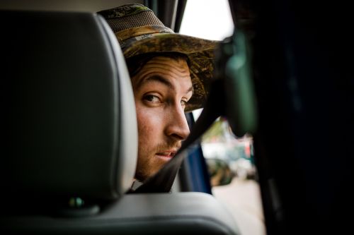 Man looks back from car seat, wearing camo hat and seatbelt, creating an eye-level portrait in natural light.