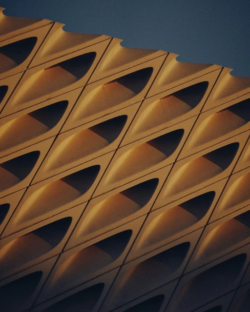 Architectural shot showcasing a building facade with a geometric pattern of repeating, concave shapes casting shadows, against a blue sky.