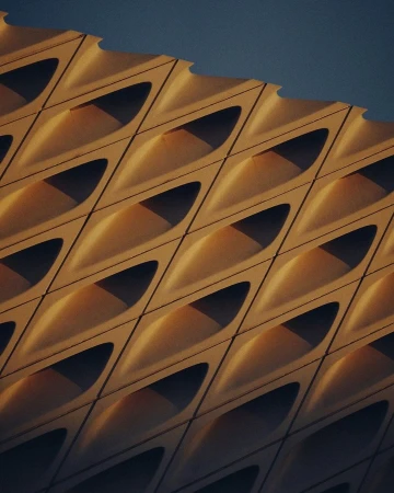 Architectural shot showcasing a building facade with a geometric pattern of repeating, concave shapes casting shadows, against a blue sky.