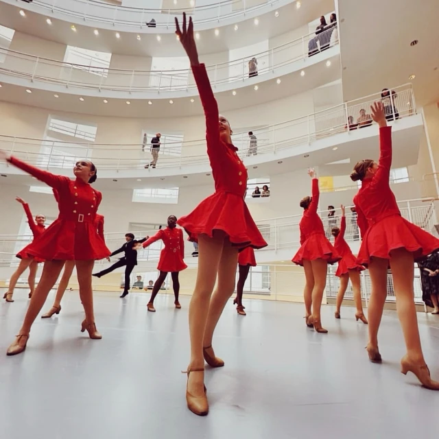A group of female dancers in red costumes are performing in the Solomon R. Guggenheim Museum in New York City, with museum visitors visible.
