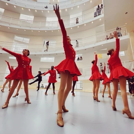 A group of female dancers in red costumes are performing in the Solomon R. Guggenheim Museum in New York City, with museum visitors visible.