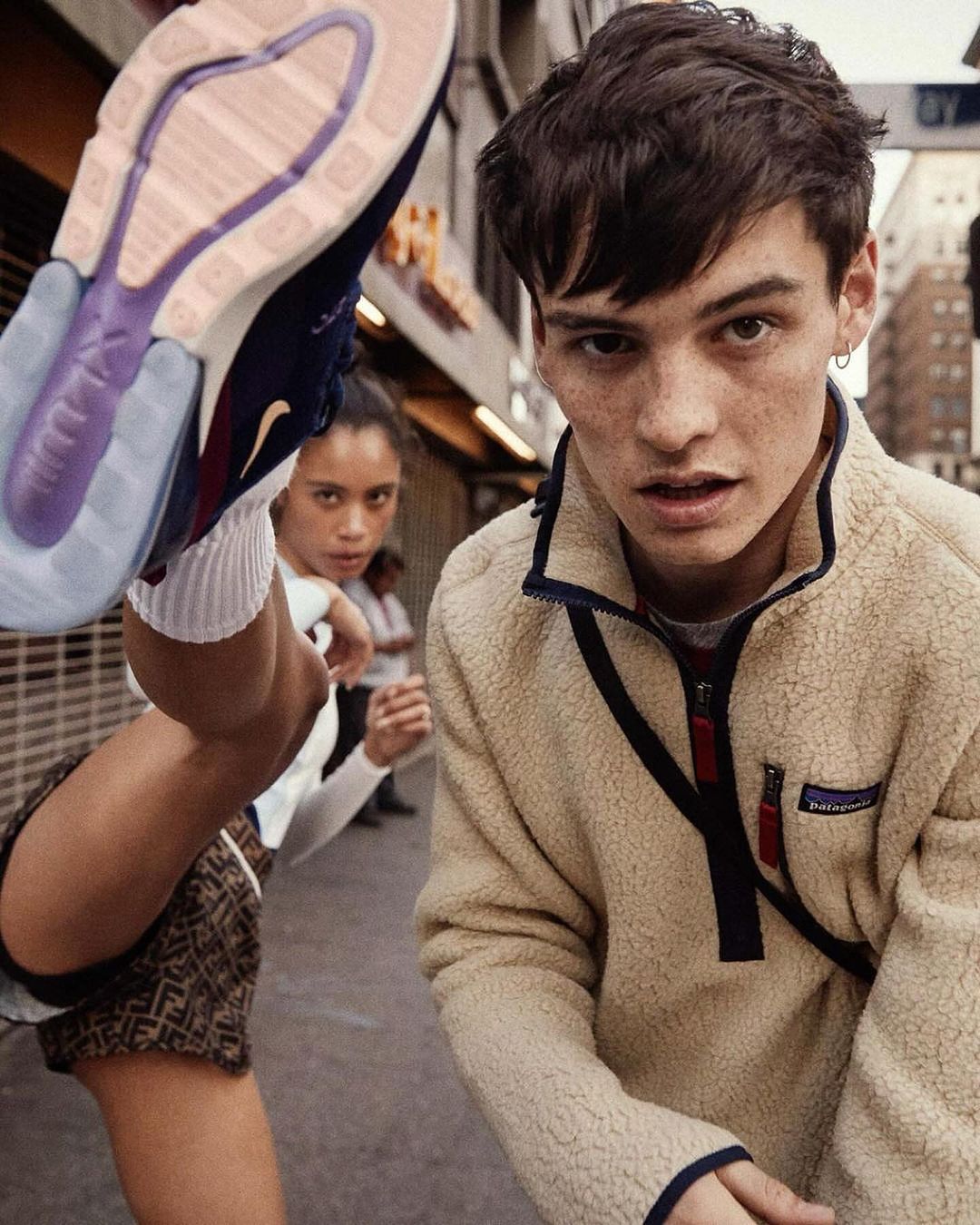 Two people pose in an urban setting. A young woman kicks her leg up, showing the bottom of a Nike Air Max 270 sneaker. A young man is facing forward.