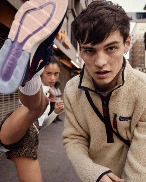 Two people pose in an urban setting. A young woman kicks her leg up, showing the bottom of a Nike Air Max 270 sneaker. A young man is facing forward.