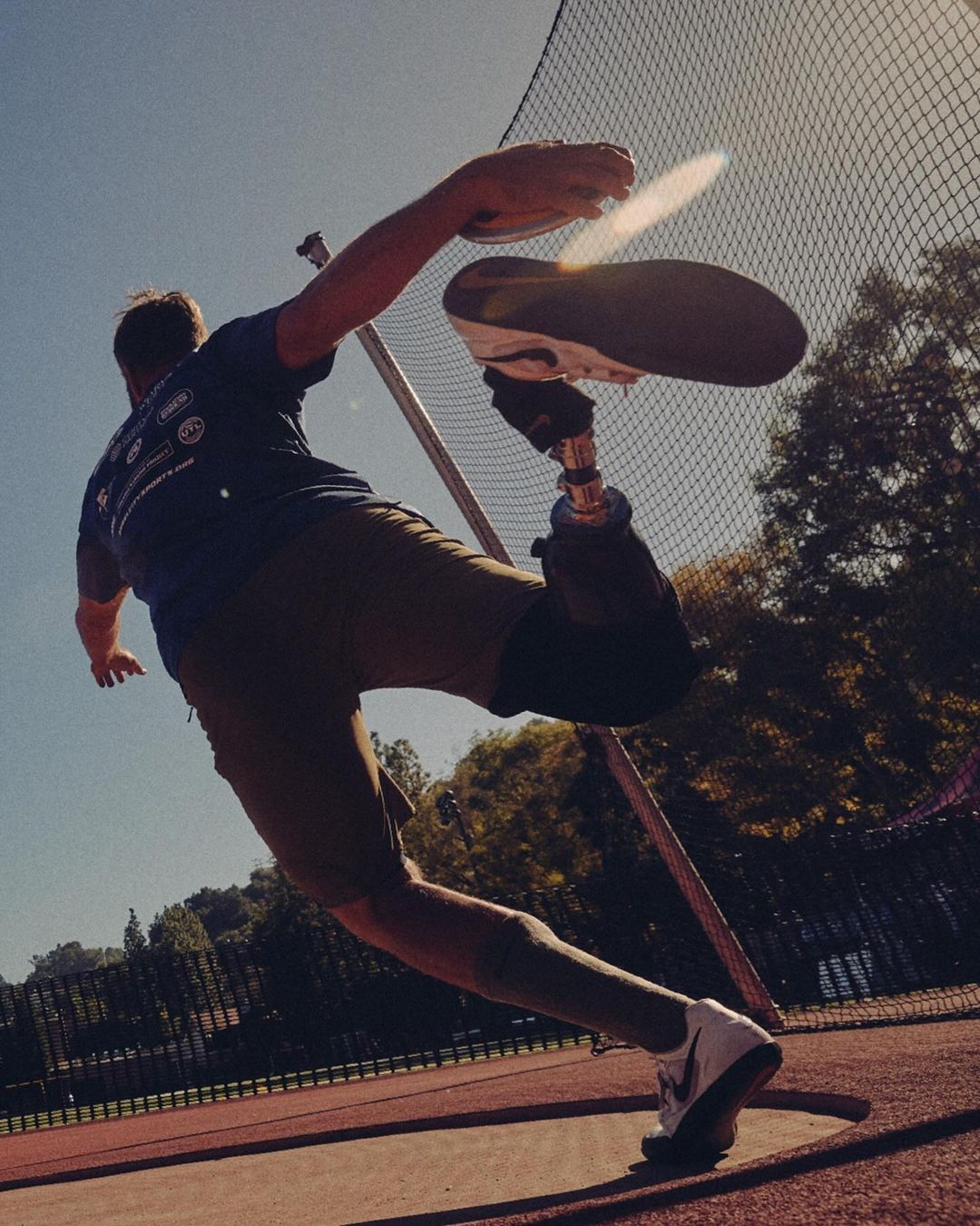 Male athlete with prosthetic leg throws a discus on a sunny outdoor track and field. Sports competition and active lifestyle concept.