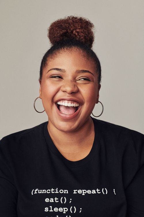 Smiling woman with hair in a high bun wearing a black graphic t-shirt against a grey background