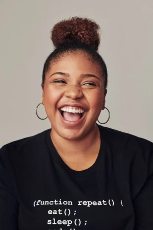 Smiling woman with hair in a high bun wearing a black graphic t-shirt against a grey background