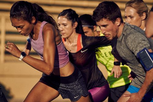 Group of adult athletes in activewear running outdoors with athletic watch and arm band visible, against a tan background in a medium shot.
