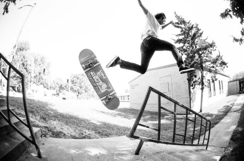 Skateboarder mid-air jumping over a rail in a black and white outdoor shot, showcasing action and skill in an urban environment.