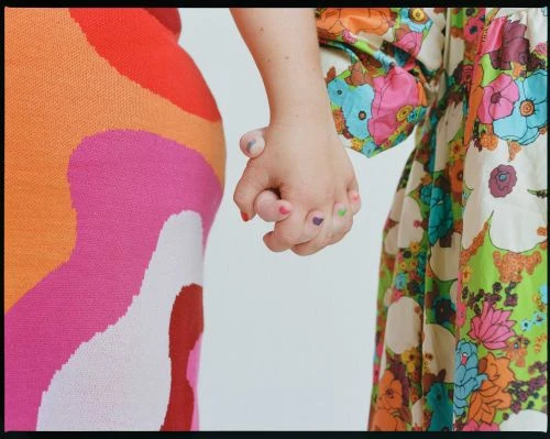 Close-up of two people holding hands, both wearing colorful, floral-patterned clothing, with focus on the hands and fabric details.