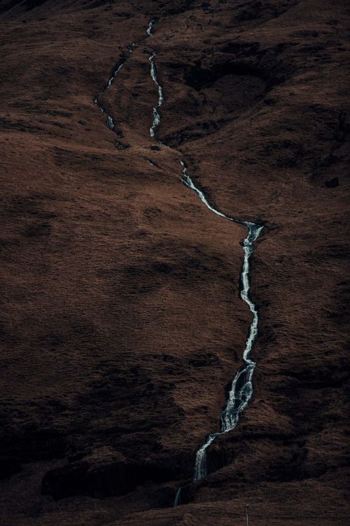 A long exposure captures a stream flowing down a hillside, showcasing blurred water motion and a dark, earthy-toned landscape.